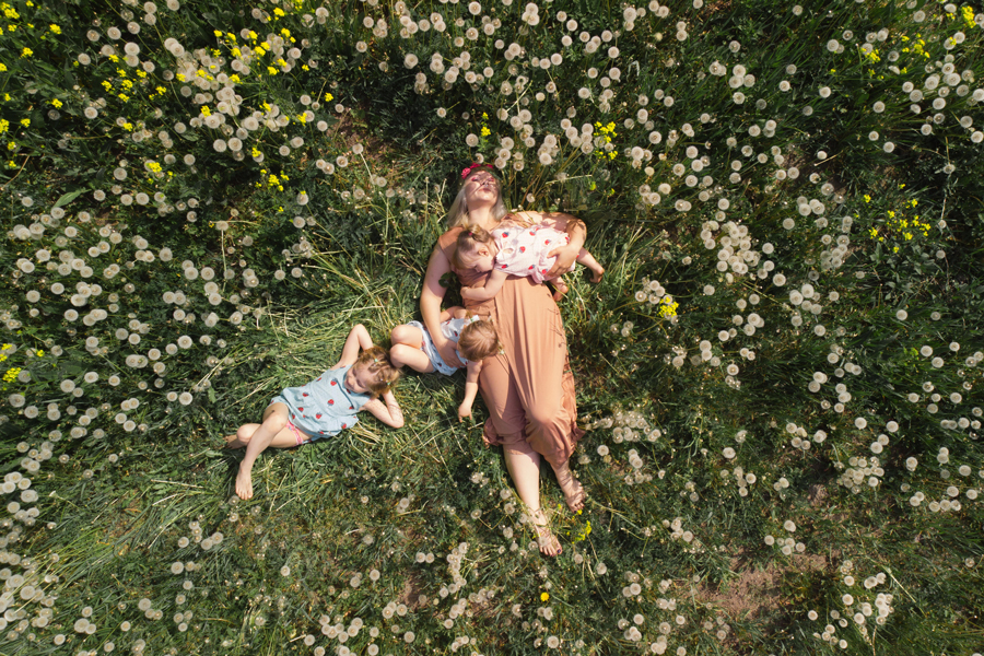 Mother seen from aerial perspective having quality playing time with her baby girls at a park blowing dandelions 